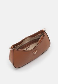 Brązowa torebka syntetyczna o gładkiej teksturze, zaokrąglonym kształcie, podwójnych zamkach błyskawicznych oraz metalowym logo na przodzie.