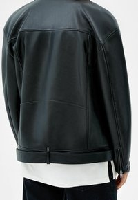 Person i svart skinnjacka med blixtlås på ärmen och vit skjorta under, visad bakifrån.