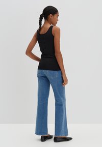 Schwarzes enges Tanktop, blaue ausgestellte Jeans und schwarze flache Schuhe. Das Top hat dünne Träger und eine glatte Textur.