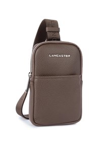 Borsa a tracolla in pelle marrone con superficie testurizzata, dotata di una tasca frontale con zip e una tracolla regolabile, marchiata "LANCASTER."