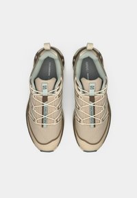 Μπεζ αθλητικά παπούτσια με άνω μέρος από διχτυωτό και συνθετικό υλικό, ελαστικά κορδόνια, λαστιχένια σόλα και ενισχυμένη μύτη. Διαθέτουν λογότυπο Salomon με μπλε λεπτομέρειες.