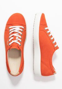Un par de zapatillas bajas de color naranja brillante con cordones blancos y suelas gruesas blancas, mostradas desde vistas superiores y laterales sobre un fondo blanco.