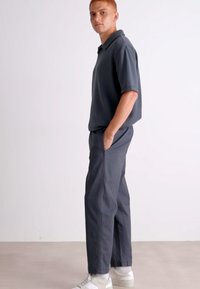 Mørk grå polo skjorte med korte ermer og rett snitt, kombinert med matchende bukser med rette ben. Brukt med hvite joggesko.