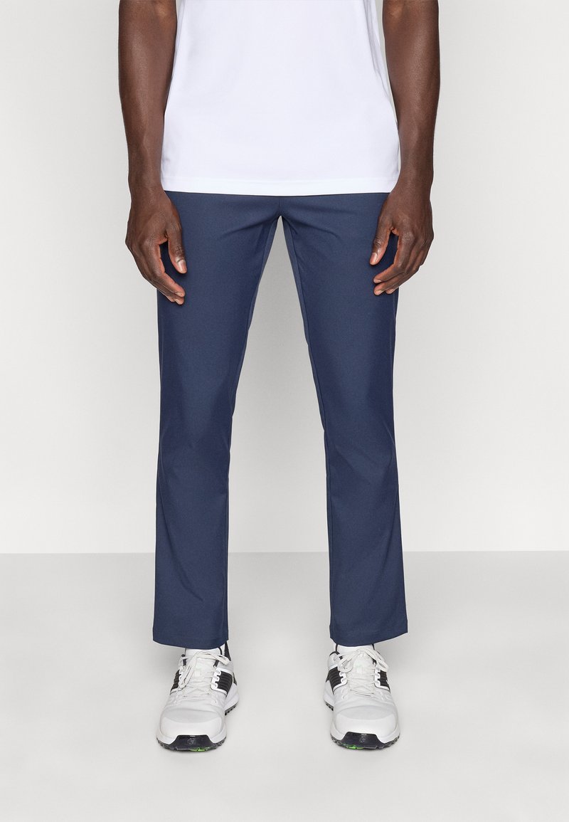 Μπλε σκούρο παντελόνι κατασκευασμένο από ελαφρύ ύφασμα με ίσια γραμμή και λεία υφή, συνδυασμένο με λευκά αθλητικά παπούτσια.
