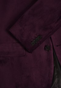 Burgundi bleiser pehmeast kangast, millel on klapiga kaelus, struktuursed õlad, neli musta nööpi mansetil ja küljetasku.