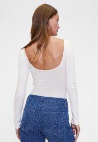Białe body z długim rękawem i odkrytymi plecami, o prążkowanej fakturze, w połączeniu z wysokim stanem niebieskich jeansów w kropki.