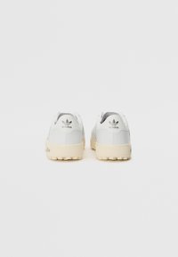Baltās Adidas kedas ar elegantu dizainu, ar struktūrētu augšdaļu, gludu papēdi un gaišas krāsas gumijas zoli ar rakstainu saķeri.