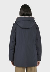 Parka bleu marine avec une capuche en fausse fourrure texturée, présentant un design mi-long, des boutons de fermeture et des poches latérales.