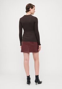 Brun langermet topp med volangkant, kombinert med en burgunder skinnminiskjørt og svarte spisse ankelstøvler. Glatt tekstur, tettsittende design.