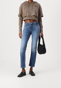 Zkrácená hnědá mikina s vyšitým znakem, v kombinaci s světle modrými rovnými džíny a texturovanou černou tkanou kabelkou. Vzhled doplňují černé mokasíny.