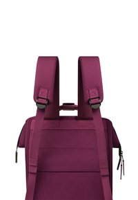 Lila Stoff-Rucksack mit gepolsterten Schultergurten, verstellbaren Schnallen und einem Tragegriff an der Oberseite; verfügt über eine strukturierte Oberfläche und eine seitliche Reißverschlusstasche.