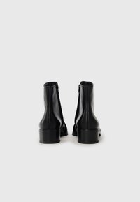 Botas de tornozelo em couro preto com um acabamento suave, bico arredondado e um salto bloco baixo. O fecho com zíper na parte de trás realça o design elegante.