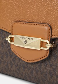 Sac en cuir beige avec une finition texturée, comportant un tissu à motif marron foncé et un fermoir doré gaufré portant la mention "Michael Kors."