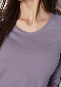 Långärmad topp i ljus lavendel, rundad halsringning, tillverkad av mjukt bomullstyg med en slät textur och minimal sömnadsdetaljer.