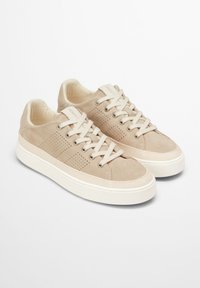 Beige suede sneakers with a perforated design, round toe, flat white rubber sole, and contrasting beige laces.