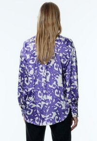 Paars en crèmekleurig blouse met een patroon, lange mouwen, knoopmanchetten en een relaxte pasvorm. Gladde stof met een glanzende afwerking.