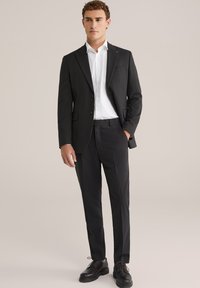 Fekete öltöny egy gombos blézerrel, fehér inggel és fekete nadrággal. A fekete bőr cipők teszik teljessé a formális megjelenést.