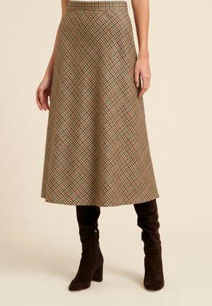 Kobieta ubrana w midi spódnicę o linii A z wysokim stanem, w kratę w kolorach brązu, beżu i zieleni, zestawioną z czarnymi zamszowymi kozakami za kolano.