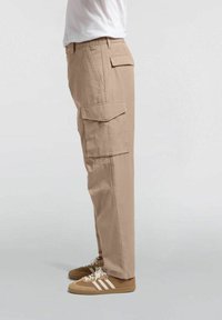 Beige cargo bukser med sidelommer og en lige skæring. Fremstillet af tekstureret stof, båret med brune sneakers med hvide striber.