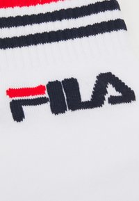 Weiße Socke mit roten und marineblauen Streifen. Verfügt über ein schwarzes, gesticktes Logo "FILA" in einer fetten, serifenlosen Schriftart. Weiche Stricktextur.