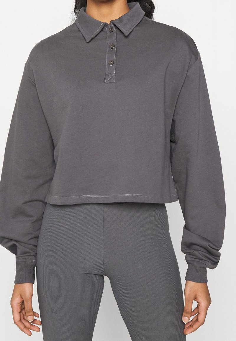 Szary skrojony pulower z kołnierzykiem, z trzema guzikami przy szyi i długimi bufkami. Miękka tkanina z widocznymi detalami szycia.