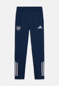 Tamsiai mėlynos sportinės kelnės su Arsenal logo, elastingu juosmeniu, dviem šoninėmis kišenėmis ir pilkais trimis dryžiais apatinėje kelnių dalyje.