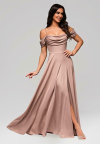 Kvinna med långt mörkt hår iklädd en mauve avaxelsklänning med hög slits och glittrande silverskor, poserande med handen på höften.