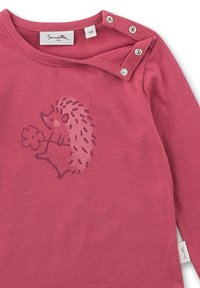 Rosa Langarmshirt aus weicher Baumwolle mit einem Igel-Motiv, der eine Blume hält. Es hat Druckknöpfe an der Schulter zum Schließen.