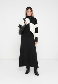 Suéter cropped tricotado em listras pretas e brancas por cima de uma saia longa preta, combinado com botas de salto pretas e uma mala de ombro preta.