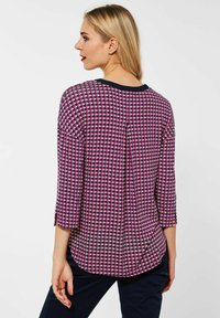 Monivärinen pusero, jossa on houndstooth-kuvio pinkissä, beigen ja laivastonsinisessä. Siinä on pyöreä pääntie ja kolmannesäinen hihat.