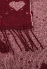 Ciorap tricotat roșu cu un model de inimi și margini franjurate. Textură moale cu puncte și inimi în nuanțe variate, creând un aspect confortabil.