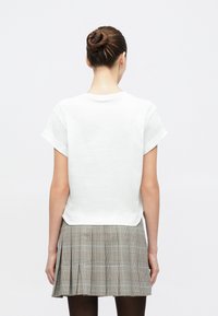 Witte katoenen T-shirt met korte opgerolde mouwen, gecombineerd met een grijze geruite plissérok. Soepele textuur, casual pasvorm.