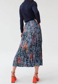 Gonna plissettata fluida in blu con vivaci motivi floreali; abbinata a una maglia a maniche lunghe blu navy e sandali con tacco a blocco arancioni.