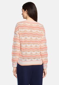 Pull en tricot avec un motif ondulé dans des teintes crème, rose et orange ; comprend un ourlet côtelé et des manches longues avec une coupe décontractée.