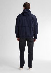 Marineblauwe windbreaker jas met een capuchon, elastische manchetten en een elastische zoom. Heeft een achterflapdetail en een eenvoudig ontwerp. Combinatie met zwarte jeans en witte schoenen.