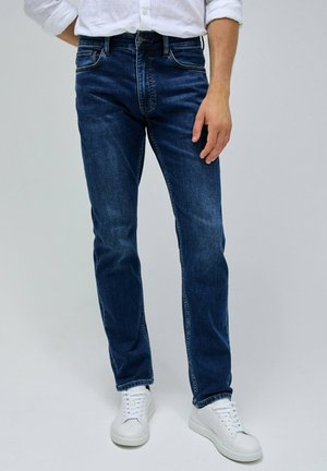 Vaqueros de mezclilla azul oscuro con un corte recto, con un ligero desgastado, cinco bolsillos y costuras en contraste. Combinados con zapatillas blancas.