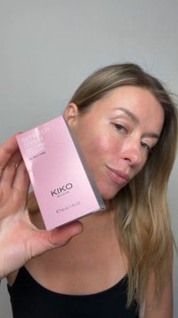 Kvinna med ljust brunt hår håller en rosa ask med KIKO Milano Skin Tech Serum Soothing Booster för alla hudtyper.