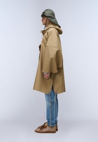 Pardesiu supradimensionat bej cu glugă, prevăzut cu închidere cu nasturi. Purtați peste blugi bleu deschis cu accente de frânghie, completați de adidași maro cu șireturi.