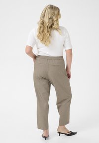 Beige, textured high-waisted trousers with a relaxed fit, side pockets, and an elastic waistband, paired with black, pointed toe heels.