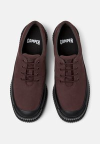 Zapatos burdeos con cordones y suelas negras, con un upper liso y un diseño sencillo, exhibidos desde una vista superior sobre un fondo blanco.