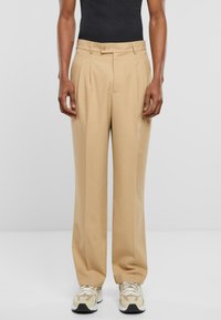 Beige, hoch taillierte Hose mit zwei vorderen Falten und einem einzigen Knopfverschluss. Der Stoff ist strukturiert; sie verfügt über seitliche Taschen und eine lockere Passform.