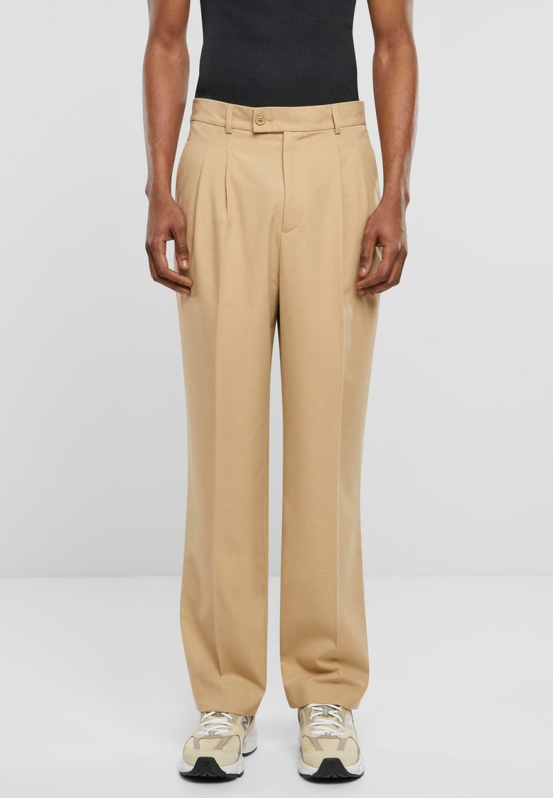 Beige, hoch taillierte Hose mit zwei vorderen Falten und einem einzigen Knopfverschluss. Der Stoff ist strukturiert; sie verfügt über seitliche Taschen und eine lockere Passform.
