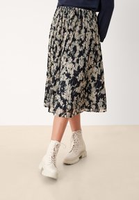 Blommig plisserad kjol i marinblått, med mönster av krämfärgade och gröna blommor. Matchas med ljusa snörade ankelskor.