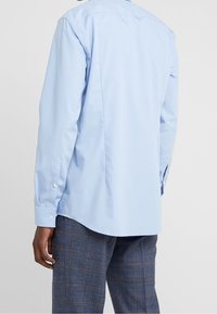 Lichtblauw, lang mouwen shirt met een rugstuk, knoopmanchetten en een afgeronde zoom. De stof lijkt soepel met een lichte glans.