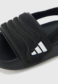 Mustast sünteetilisest materjalist liug-sandaal, mille pealispind on tekstuuriga ja paralleelsete soontega ning millel on kontrastne logoga dekoratsioon.