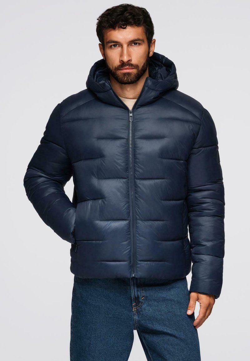 Giacca a vento navy con cappuccio, caratterizzata da baffle orizzontali, zip frontale e polsini elasticizzati, abbinata a jeans in denim.