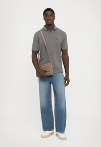Szürke poloing kontrasztos gallér részletekkel, világoskék egyenes szárú farmernadrággal és krémszínű sportcipőkkel párosítva. Egy barna crossbody táska is tartozik hozzá.
