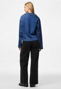 Tumši zila džinsu jaka ar apkakles izgriezumu un īsu griezumu, apvienota ar augsta vidukļa melnām biksēm un melnu apavu.