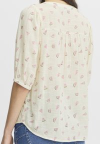 Lichtgele blouse met een textuurstof en een patroon van kleine roze watermeloenschijven en groene schilaccenten. Elastische mouwen.
