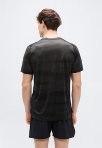 Μαύρο αθλητικό πουκάμισο με κοντά μανίκια και υφή, στρογγυλή λαιμόκοψη και ανοίγματα στα πλάγια, φορεμένο με μαύρο σορτς. Εμφανίζεται η πίσω όψη.